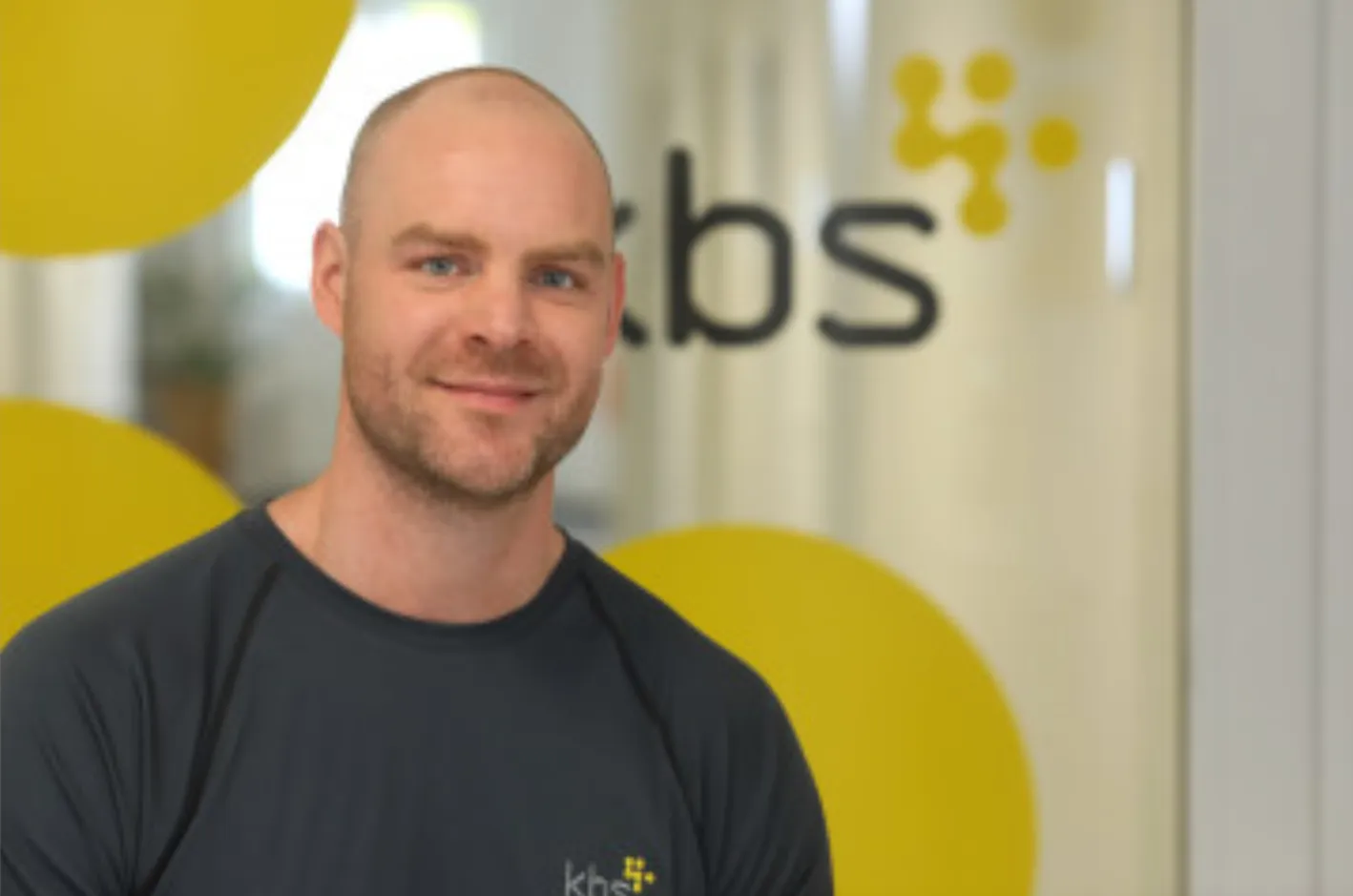 Sebastian Flüter vor dem Logo der kbs — Die Akademie für Gesundheitsberufe